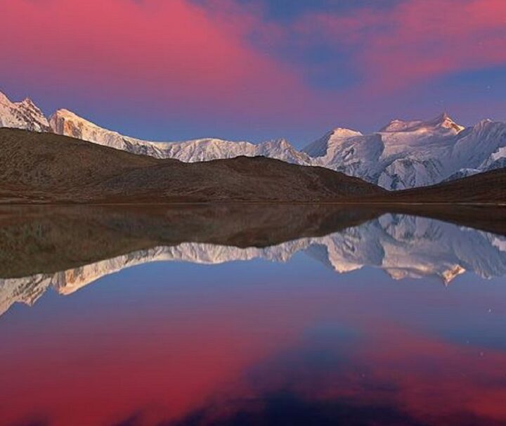 Rush Lake in Hunza reflecting snow-capped peaks under a stunning sunset sky.